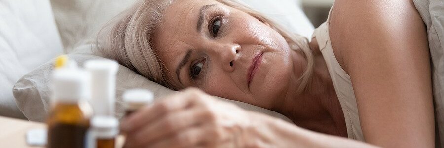 An elderly woman lying in bed looks at a selection of sleeping pills